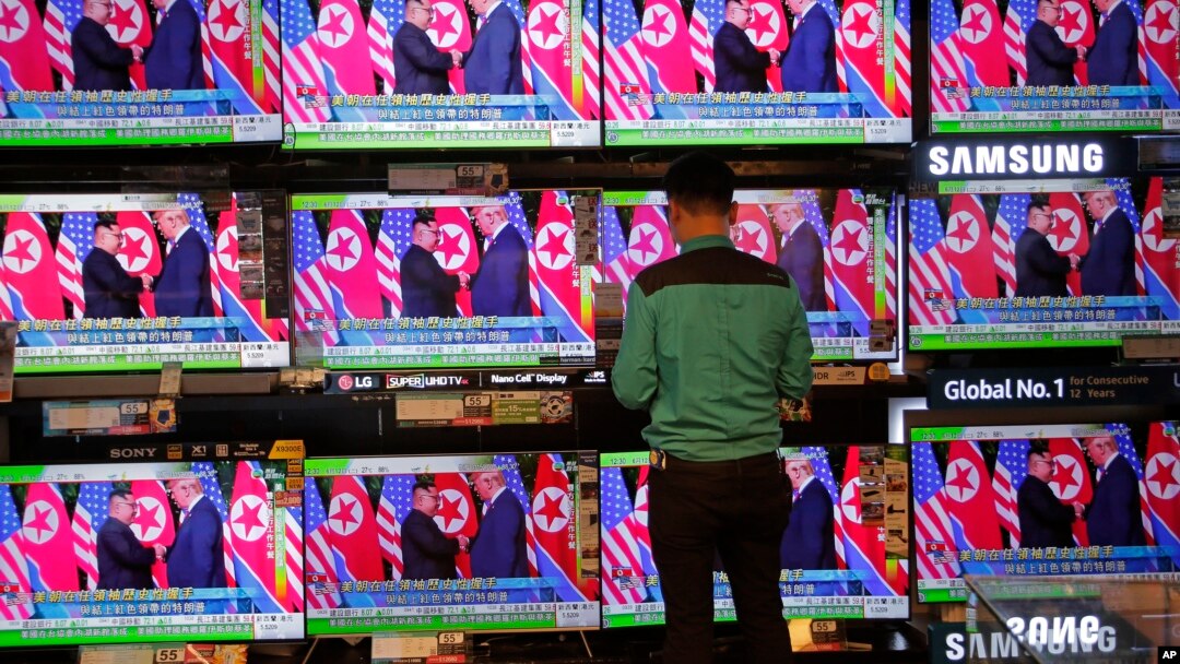 A man watches TV screens showing U.S. President Donald Trump, right, meeting with North Korean leader Kim Jong Un in Singapore, during a news program In Hong Kong, June 12, 2018.