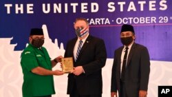 Menlu AS Mike Pompeo (tengah) menerima kenang-kenang dari Ketua Umum Pimpinan Pusat Gerakan Pemuda Ansor Yaqut Cholil Qoumas (kiri), didampingi Sekjen Nahdlatul Ulama, Yahya Cholil Staquf, di Nahdlatul Ulama, Jakarta, 29 Oktober 2020. (Adek Berry/Pool Photo via AP).