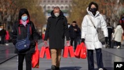 FILE - Residents wearing face masks carry their purchased Lunar New Year goodies at Qianmen Street, a popular tourist spot in Beijing, Jan. 17, 2023. 