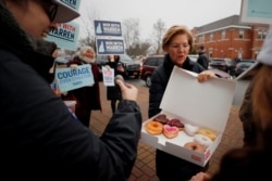 FILE - Democratic presidential candidate Sen. Elizabeth Warren of Massachusetts offers donuts to supporters at a polling site for New Hampshire’s first-in-the-nation primary in Portsmouth, N.H., Feb. 11, 2020.
