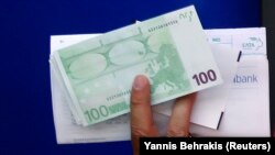 Foto ilutrasi menunjukkan sebuah tangan yang memegang uang Euro yang baru ditarik dari sebuah mesin ATM di Athena, Yunani, pada 13 Juni 2012. (Foto: Reuters/Yannis Behrakis)