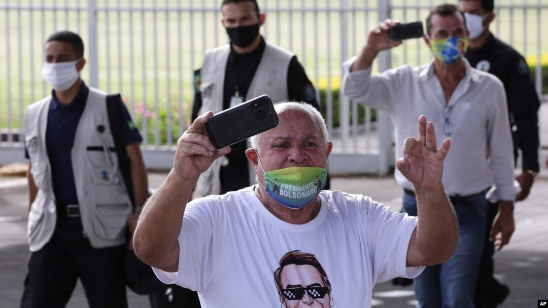 A supporter of Brazil's President Jair Bolsonaro, wearing a T-shirt covered in pro-Bolsonaro messages, yells at journalists after the president's departure from his official residence of Alvorada palace in Brasilia, May 25, 2020. 