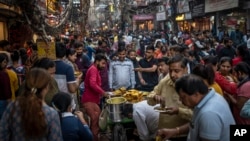 FILE - People eat street food as shoppers crowd a market in New Delhi, India, Saturday, Nov. 12, 2022. The world's population is projected to hit an estimated 8 billion people on Tuesday, Nov. 15, according to a United Nations projection. (AP Photo/Altaf Qadri, File)