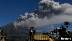 Seorang pria menggendong anaknya di kebun jagung desa Sibintun, kabupaten Karo, Sumatera Utara, dengan latar belakang asap dari Gunung Sinabung. (Foto: Dok)