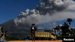 Seorang pria di desa Sibbintun distrik Karo nampak menggendong anaknya sambil berjalan di ladangnya yang kerning, sementara gunung Sinabung kembali mengeluarkan asap dan gas (25/11).