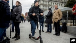 In this Dec. 4, 2018, photo a man rides a scooter near the White House in Washington. Electric scooters are overtaking station-based bicycles as the most popular form of shared transportation outside transit and cars. (AP Photo/Andrew Harnik)