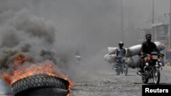 Men riding motorbikes pass next to a burning tire at a barricade in a street of Port-au-Prince, Haiti, Oct. 2, 2019.