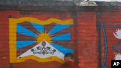 Seorang biksu Tibet di pengasingan berdiri di depan dinding yang dicat dengan bendera Tibet di Katmandu. (Foto: AP)