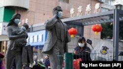 A woman wearing a mask walks past statues with masks placed on them in Wuhan in central China's Hubei province on Friday, Jan. 29, 2021. A World Health Organization team is visiting the central city of Wuhan where the coronavirus was first detected. (AP Photo/Ng Han Guan)