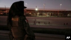 FILE - A female soldier watches over the Mexican side of the border during an artist protest on the border of Mexico and the U.S., in Ciudad Juarez, Mexico, Sept. 28, 2019.