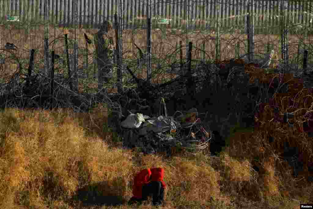 A migrant sits near near a razor wire fence, set by U.S. authorities to inhibit the crossing, as a member of the Texas National Guard operates in Ciudad Juarez, Mexico.