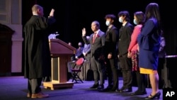 In this photo provided by Peg Shanahan, Lowell District Court Judge Stephen Geary, left, swears in new Cambodian-American Mayor Sokhary Chau, Monday, Jan. 3, 2022, in Lowell, Massachusetts, as Chau's family stands with him. 