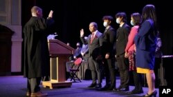 In this photo provided by Peg Shanahan, Lowell District Court Judge Stephen Geary, left, swears in new Mayor Sokhary Chau during the Lowell City Council swearing-in ceremony, Monday, Jan. 3, 2022, in Lowell, Mass., as Chau's family stands with him. (Peg Shanahan via AP)