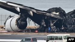 Officials look at the burnt wreckage of a Japan Airlines passenger plane on the tarmac at Tokyo International Airport at Haneda in Tokyo on Jan. 3, 2024, the morning after the JAL airliner hit a smaller coast guard plane on the ground.