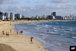 FILE — Beachgoers walk along South Beach, March 15, 2020, in Miami Beach, Florida. (AP Photo/Lynne Sladky, File)