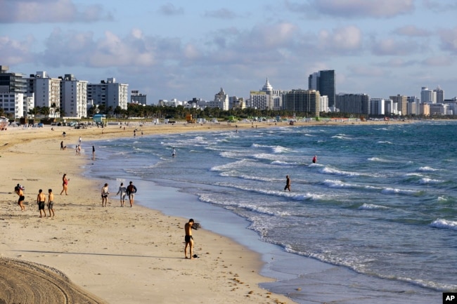 FILE — Beachgoers walk along South Beach, March 15, 2020, in Miami Beach, Florida. (AP Photo/Lynne Sladky, File)