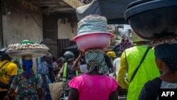 FILE - Women carry goods on their head as they walk in the Dantokpa market, one of the largest open-air market in West Africa, in Cotonou, Benin, on Feb. 29, 2024. 