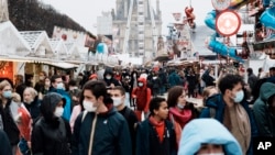 FILE - People wear face masks to curb the spread of the coronavirus as they walk in the alley of a funfair in Paris, France, Dec. 29, 2021.