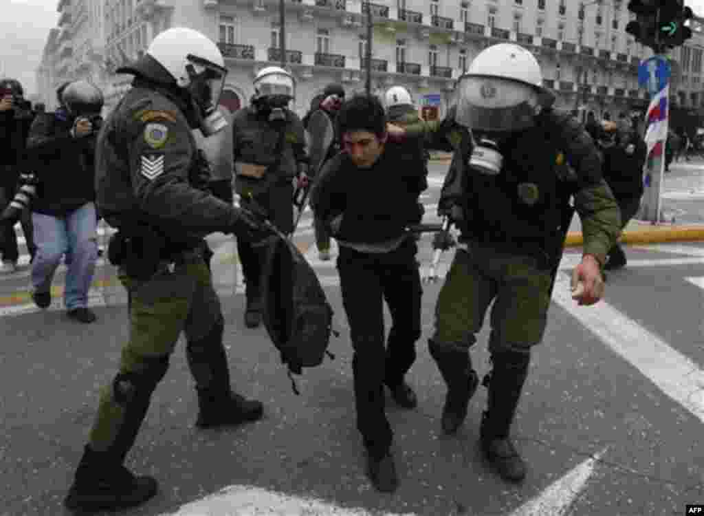A riot policeman, right, detains a protester while another, left, holds a bag from which an arrow protrudes during clashes in Athens, Wednesday, Feb. 23, 2011. Scores of youths hurled rocks and petrol bombs at riot police after clashes broke out Wednesday