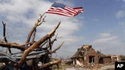 A United States flag tied to a tree branch waves in the wind over a business building destroyed by a tornado in Joplin, Missouri. Search teams accompanied by cadaver dogs on Tuesday picked their way through the rubble of thousands of homes and businesses 