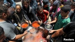 Palestinianos reúnem-se para receber alimentos confeccionados por uma cozinha de caridade, em Khan Younis.