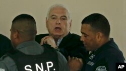 El ex presidente panameño Ricardo Martinelli es escoltado esposado durante un receso en su audiencia en la Corte Suprema de la Ciudad de Panamá, el miércoles 27 de junio de 2018. Martinelli fue extraditado de Estados Unidos para enfrentar cargos de espionaje político y malversación de fondos. (AP Photo / Arnulfo Franco)