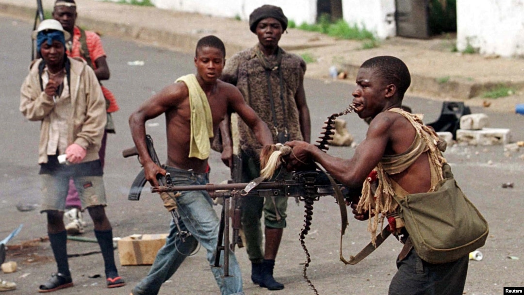 FILE - May 8, 1996 photo shows a street fighter with Charles Taylor's NPFL firing his machine gun while holding the string of bullets in his teeth during a heavy exchange.