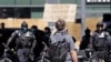 A protester holds up a sign toward police officers Sunday, July 26, 2020, in Seattle, where a small group of demonstrators gathered to protest against Immigration and Customs Enforcement.