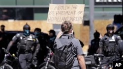 A protester holds up a sign toward police officers Sunday, July 26, 2020, in Seattle, where a small group of demonstrators gathered to protest against Immigration and Customs Enforcement.