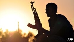 FILE - A fighter from the Kurdish People Protection Unit (YPG) poses for a photo at sunset in the Syrian town of Ain Issi, some 50 kilometres north of Raqqa, uring clashes between IS group jihadists and YPG fighters on July 10, 2015. 