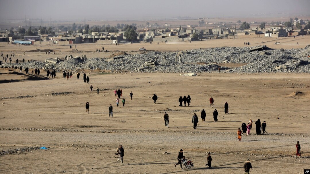 Iraqi citizens who fled the fighting between the Islamic State militants and the Iraqi forces, walk in front of destroyed houses on their way to receive aid supplies and clothes, in the Samah front line neighborhood, in Mosul, Iraq, Nov. 28, 2016. The off