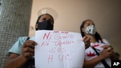 La trabajadora del Hospital Universitario Yenifer Esculpi sostiene un cartel que dice "sin guantes, sin mascarillas. SOS", durante una protesta en Caracas, el 7 de abril de 2021. [Foto: AP].