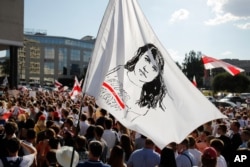 People hold a flag with a portrait of Sviatlana Tsikhanouskaya, main opposition candidate in presidential elections, during a rally contesting the official poll results, in Minsk, Belarus, Aug. 17, 2020.