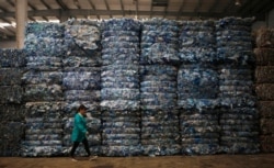 FILE - A worker walks past piles of plastic PET bottles at Asia's largest PET plastic recycling factory INCOM Resources Recovery in Beijing, China, May 7, 2013.