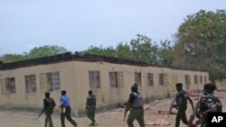 FILE - Security guards walk past a burned-out government secondary school in Chibok, Nigeria. April, 21. 2014.