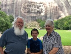 FILE - Paula and Michael Smith pose for a photo with their grandson, Evan, 10, in front of a giant carving of Confederate figures during a visit to Stone Mountain Park, June 29, 2020.