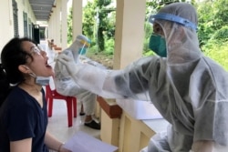 FILE - A medical specialist wearing protective suits takes a swab sample to test for COVID-19 from a woman at a military base in southern Mekong delta Dong Thap province, Vietnam, August 8, 2020.