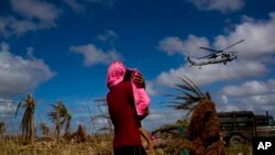 Seorang korban topan Haiyan yang selamat berdiri menggendong anaknya sambil melihat helikopter yang terbang rendah yang membawa bantuan untuk para korban bencana di Guiuan, Pulau Samar, Filipina.