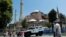 FILE - Tourists enter the Byzantine-era monument of Hagia Sophia as they pass by an armored police vehicle in the Old City of Istanbul, Turkey, July 13, 2016.