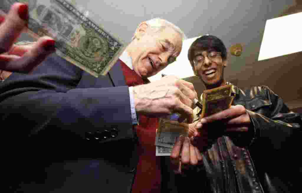 Ron Paul menandatangani namanya pada selembar uang dolar pada malam kaukus di Minnesota di Coon Rapids, Minnesota (7/2) (REUTERS).