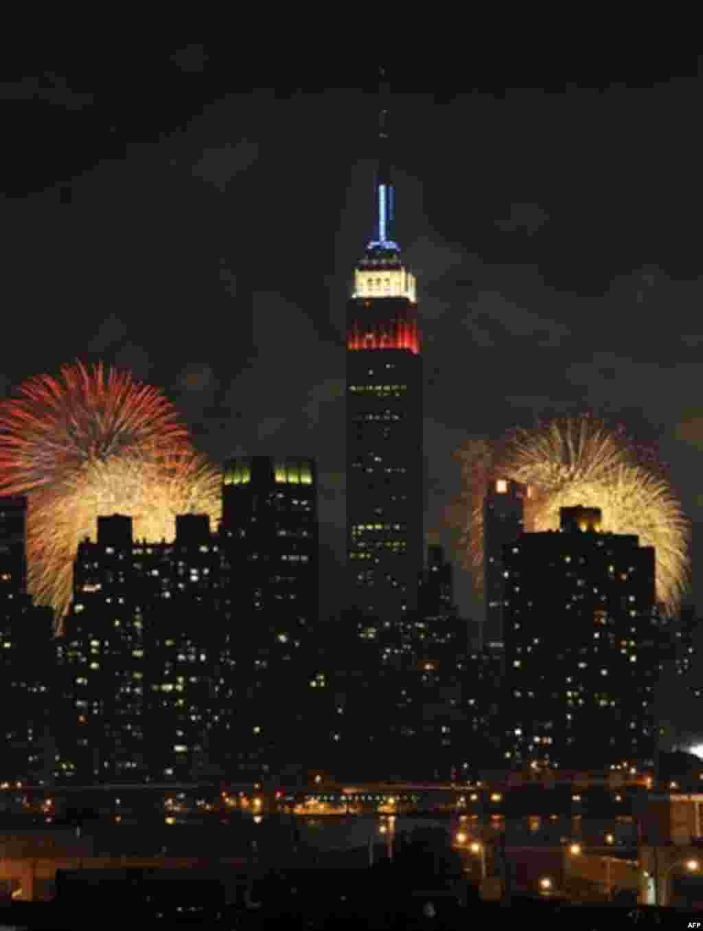 The Empire State Building, illuminated with red, white and blue lights, is seen from across the East River in the Queens borough of New York, as fireworks exploding over the Hudson River during the Macy's Fourth of July fireworks show on Monday, July 4, 2