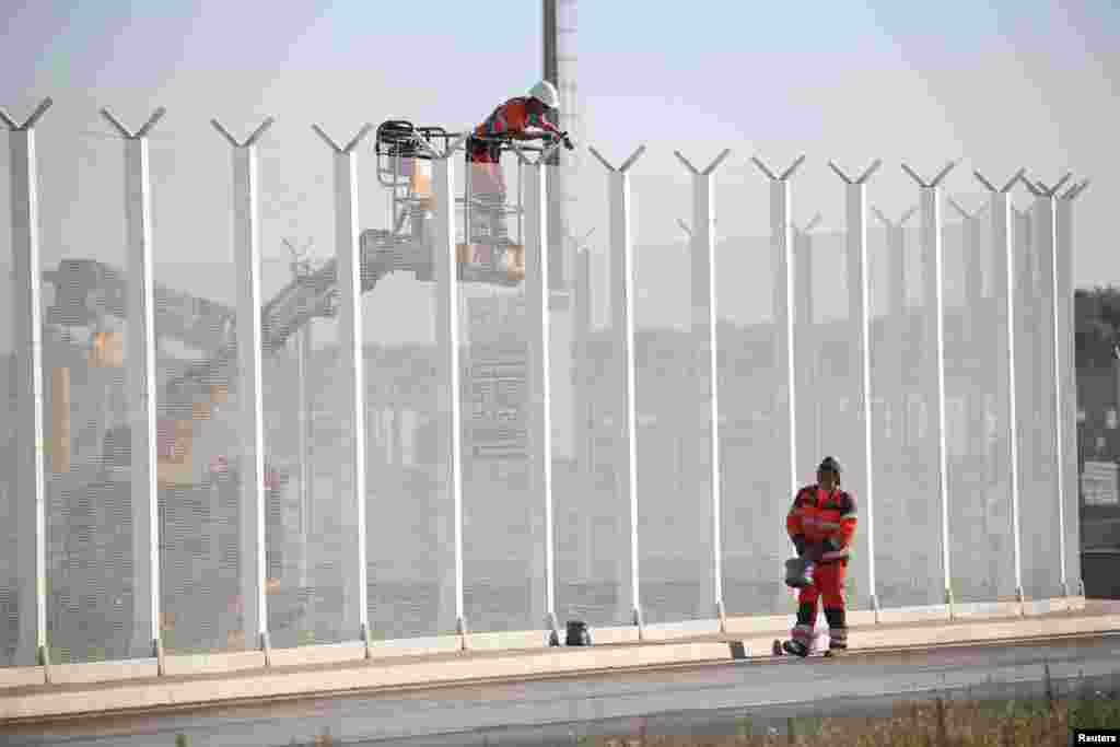 Workers set-up barbed wires on top of a fence along the harbor of Calais to prevent migrants jumping aboard lorries, France.