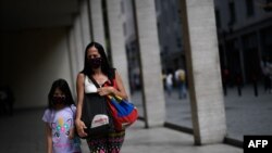 Una mujer y una niña usan tapabocas mientras caminan por el centro de Caracas después que el gobierno alivió el confinamiento nacional que impuso como medida preventiva contra la COVID-19.