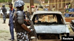 A policeman stands near damaged vehicles after a suicide car bomber killed five people on a street of popular bars and restaurants in Sabon Gari, Kano, Nigeria, May 19, 2014.