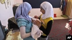 Syrian girls, who fled their home in Anadan with their family hold their relative Mohammed Mustafa who was born five days ago in a school in Kafar Hamra, Syria, August 22, 2012.