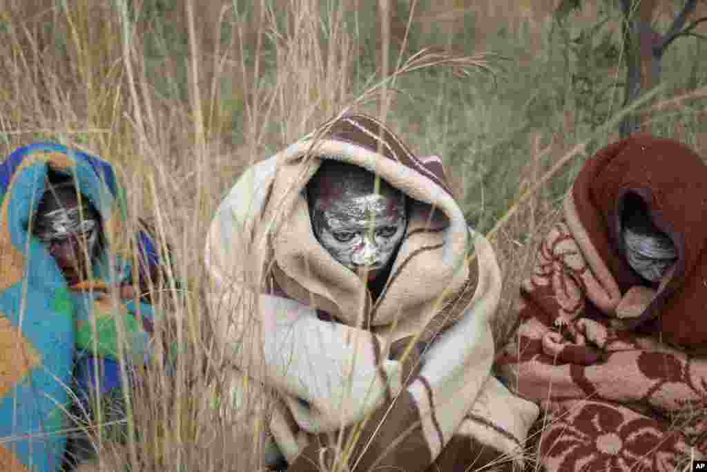 Xhosa boys covered with blankets and smeared with chalky mud sit in a field as others undergo a traditional male circumcision ceremony in Qunu, South Africa.