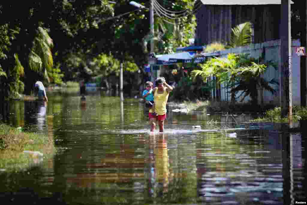 Seorang perempuan menggendong anak sambil mengarungi banjir di Acapulco (18/9). (Reuters/Jacobo Garcia)