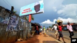 People walk past a campaign poster for incumbent President Ernest Bai Koroma, in Freetown, Sierra Leone, October 19, 2012. 