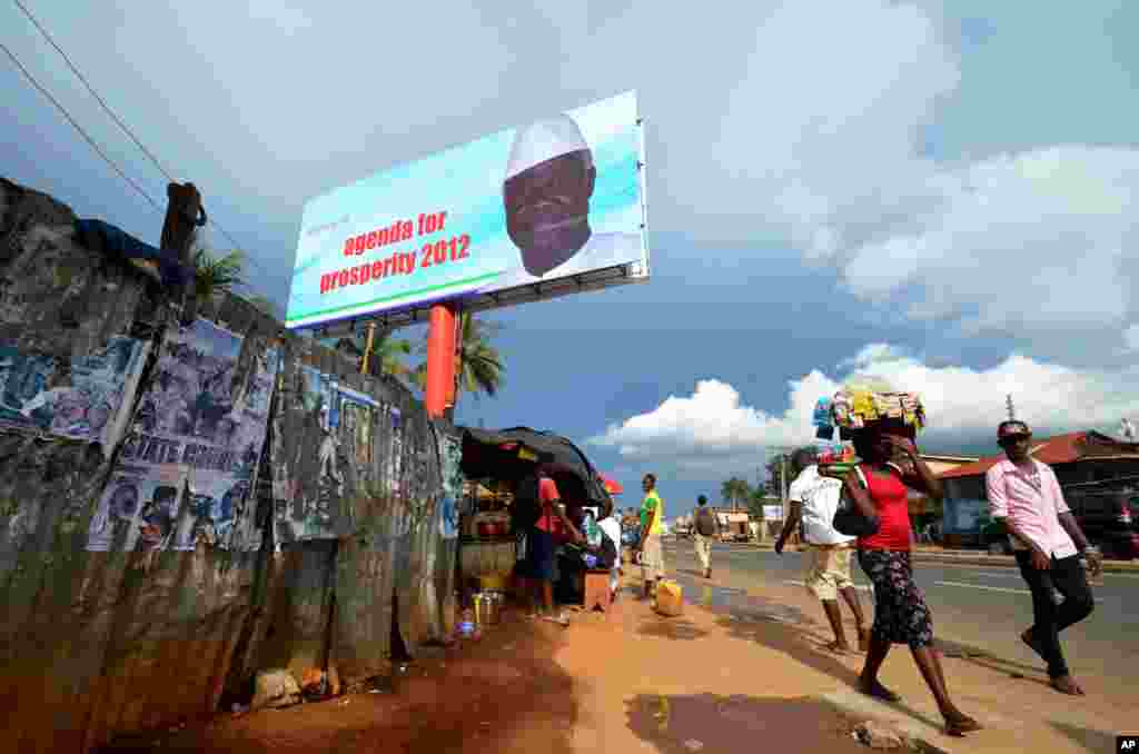 People walk past a campaign poster for incumbent President Ernest Bai Koroma, in Freetown, Sierra Leone, Oct. 19, 2012. 