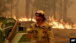 A Forest Corporation worker manages a fire hose as he battles a fire near Moruya, Australia, Jan. 4, 2020. Australia's Prime Minister Scott Morrison called up about 3,000 reservists as the threat of wildfires escalated Saturday in at least three states.